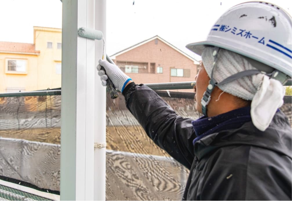 冬の屋外で柱の塗装を行う職人の写真。