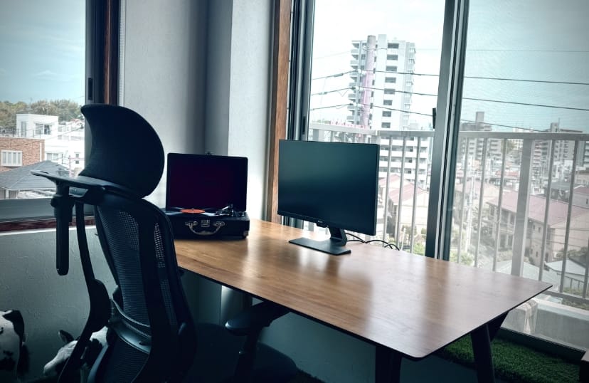 写真:ストレンジブレイン株式会社事務所内。大きな窓に向かった木製デスクにパソコンのモニターが置かれている。